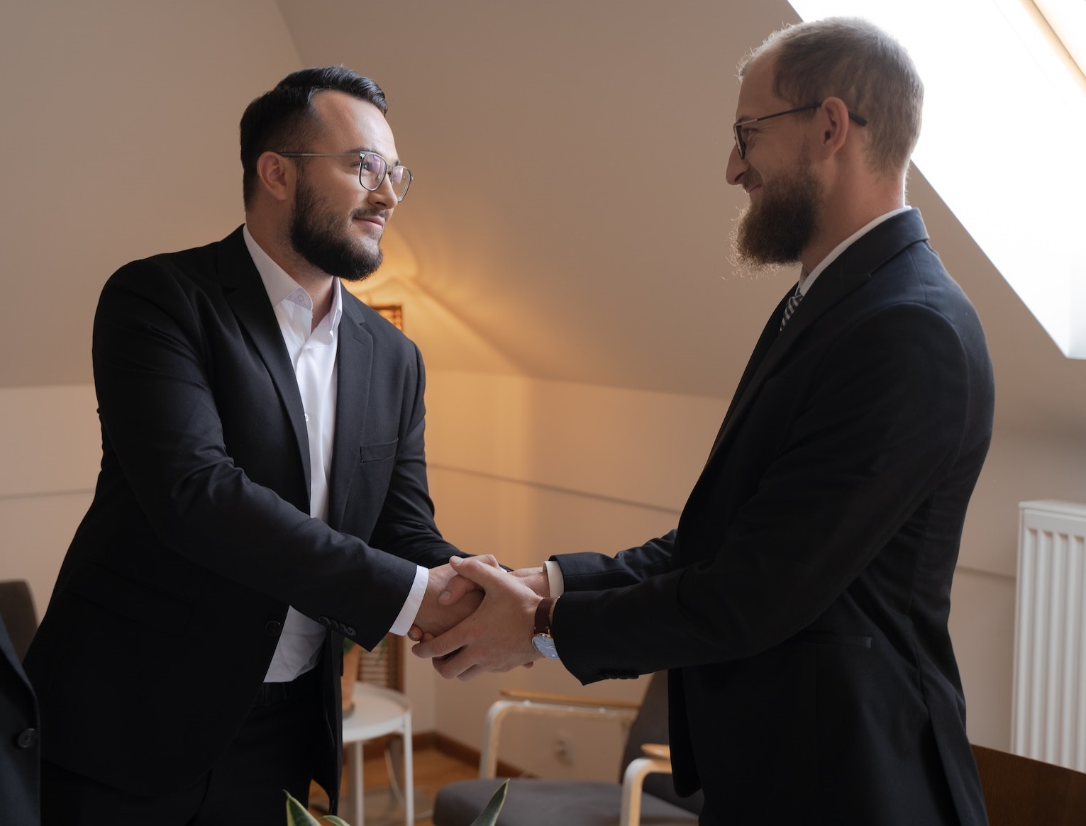 Two man in suits are talking and shaking hands in office.