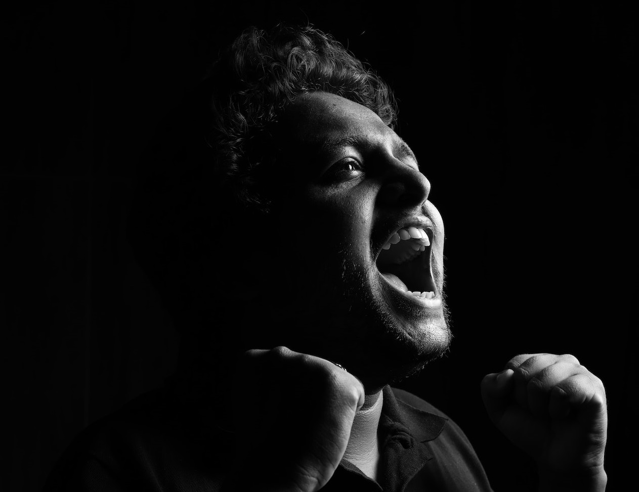 Young man with closed fists is yelling alone.