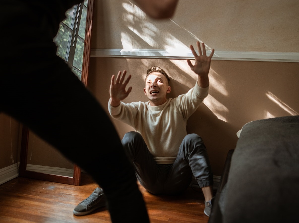 Young man is seating on the wooden floor with arms up and scared face.