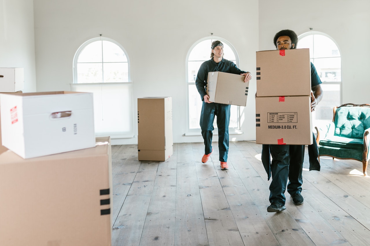Two men are carrying boxes inside of the house.