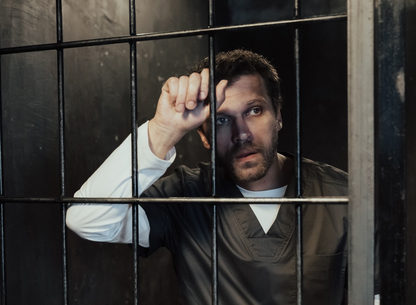 Man wearing black jumpsuit is looking from jail cell.