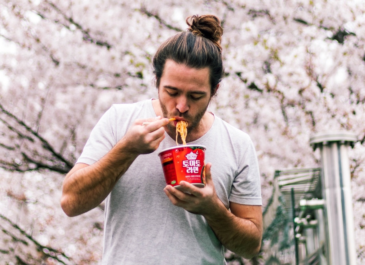 Young man wearing white shirt is eating a noodles outside.