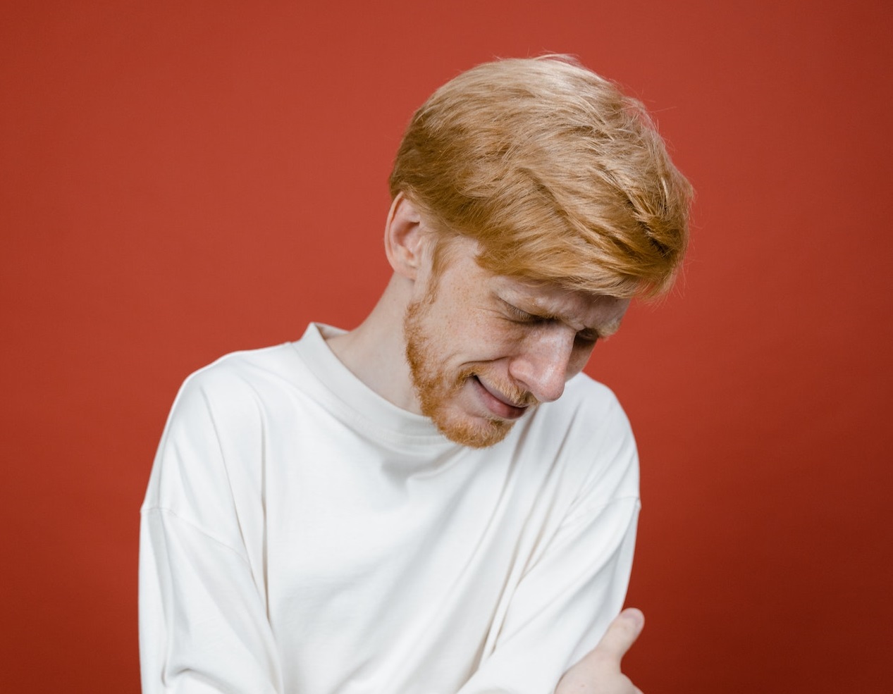 Sad man wearing white shirt is crying and looking down.