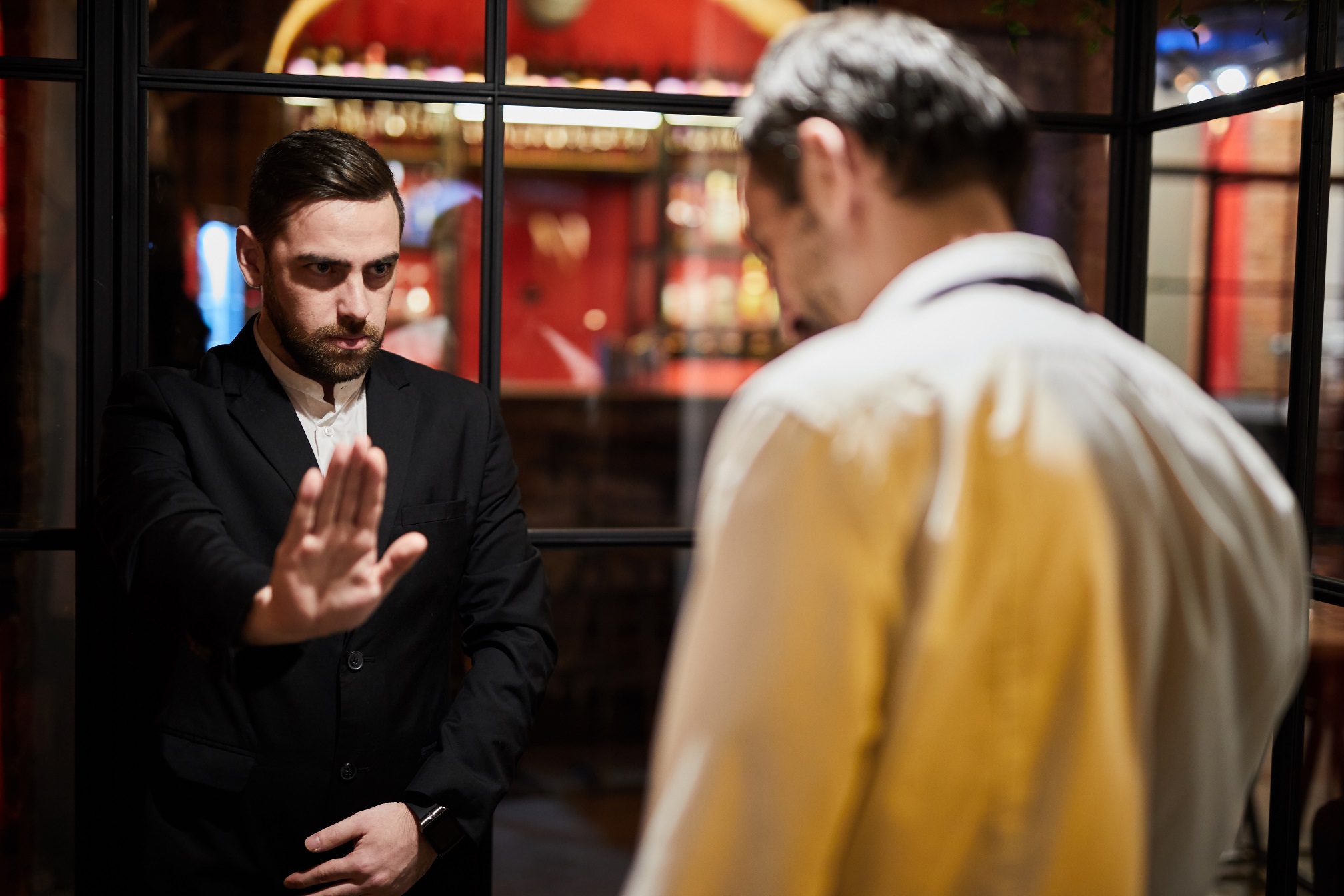 Security guard stopping waiter man from entering at luxury establishment.