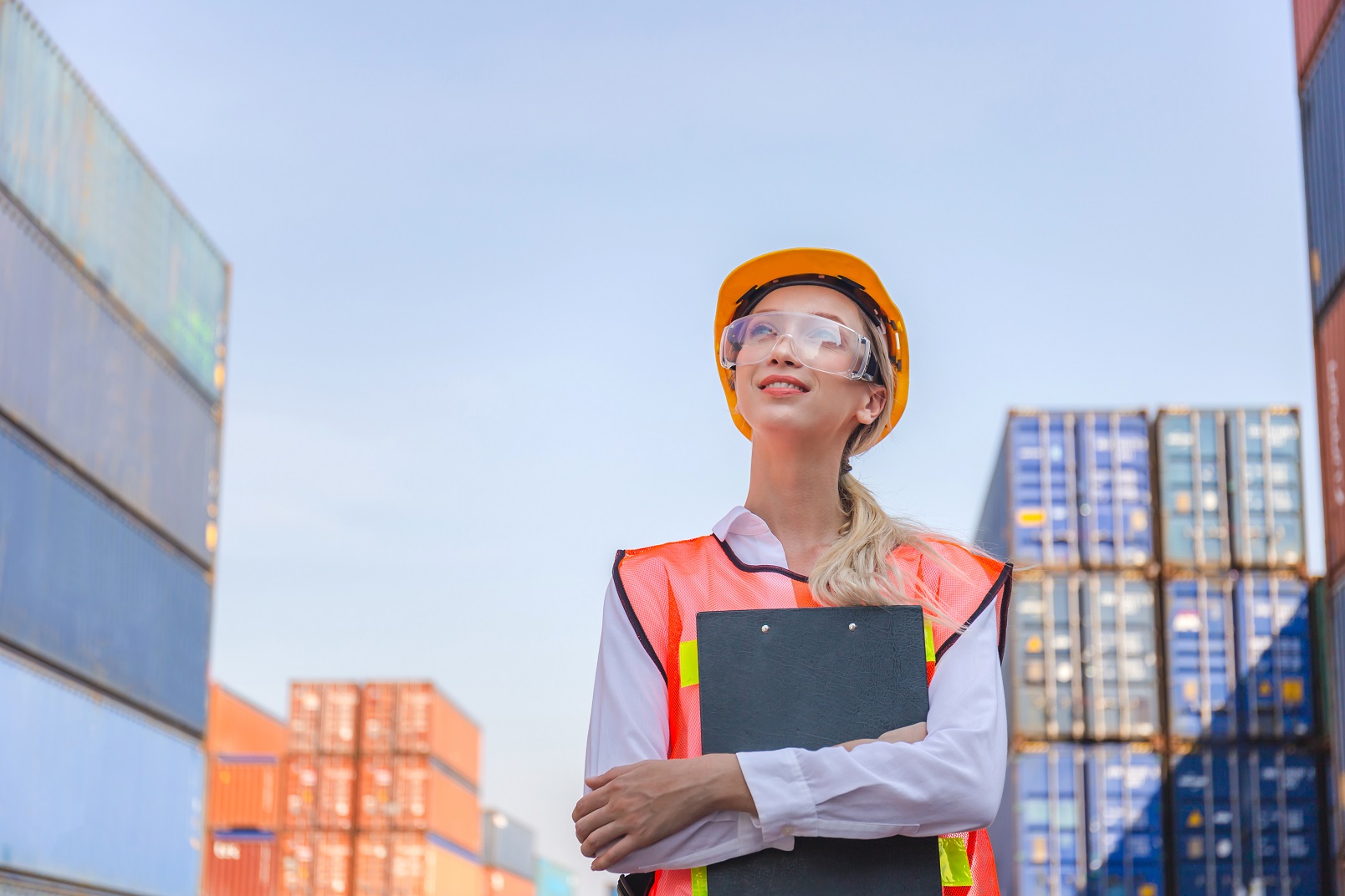 Young woman is looking up to shipping containers and smiling.