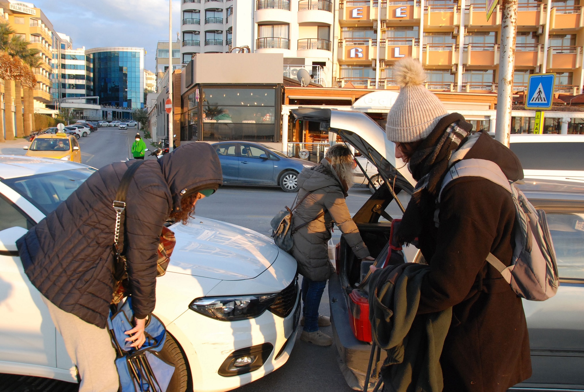 People are putting their luggage in back of a car.