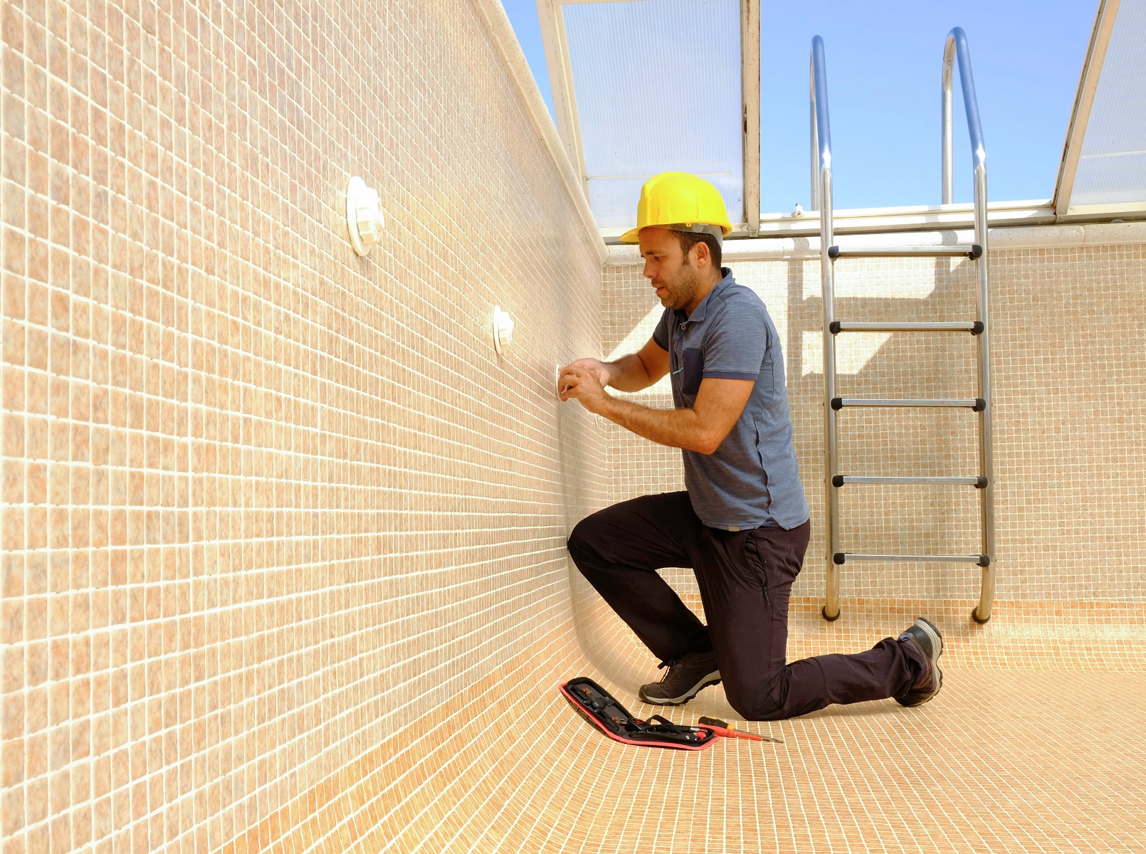 Worker is installing pool ladder in an empty swimming pool.