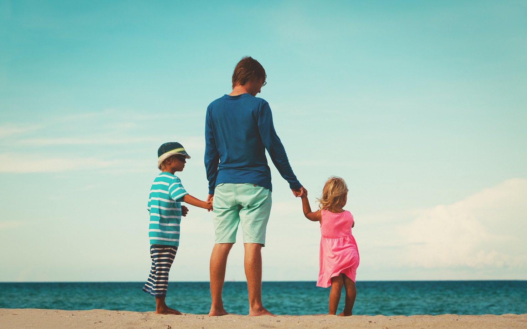 Father is standing on the beach with two kids.