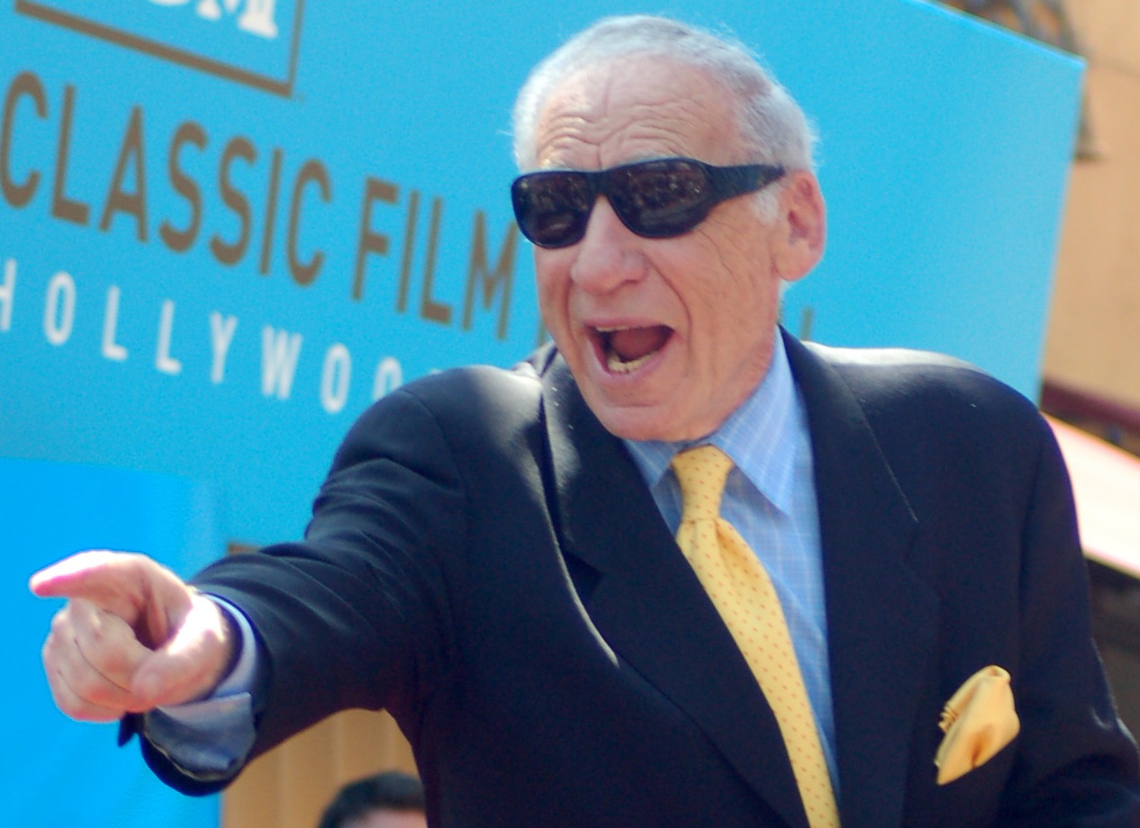Mel Brooks wearing black shirt and yellow tie on black suit yelling and pointing on side - 2010