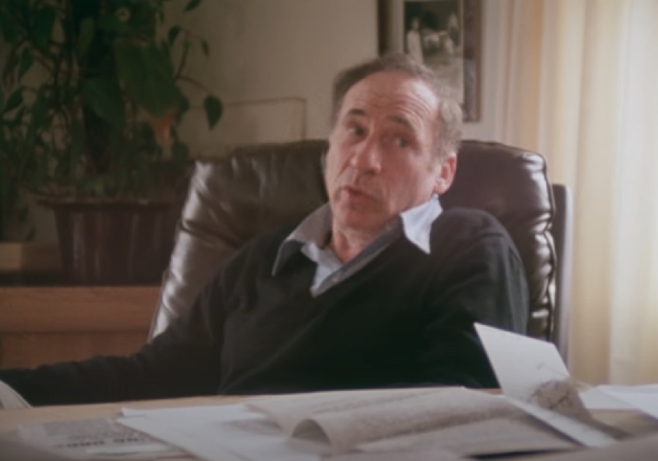 Screenshot: Mel Brooks is seating on desk and looking at side - from Mel Brooks-Unwrapped (2018)