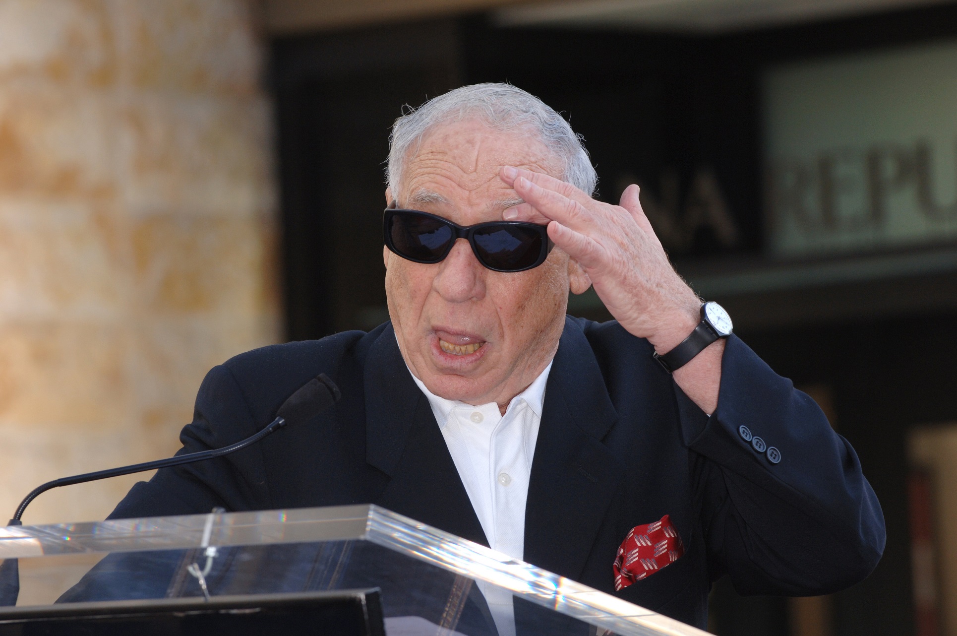 Mel Brooks wearing black suit and sunglasses is standing with open mouth in front of people - 2006
