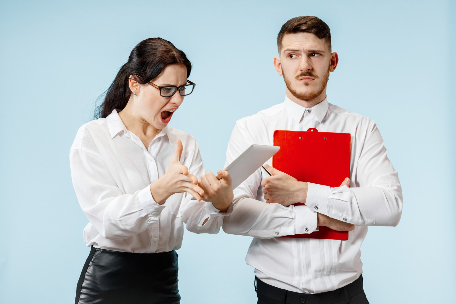 Young woman is holding a tablet and yelling to a young male who is looking surprised at her.