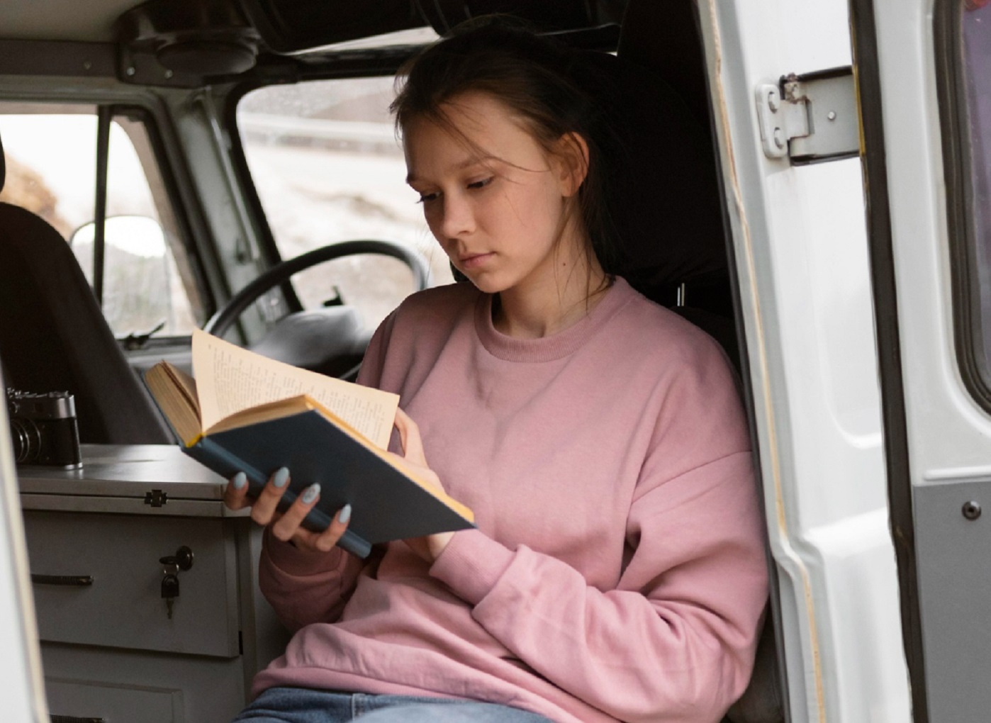 Young woman is reading a book inside a white van.