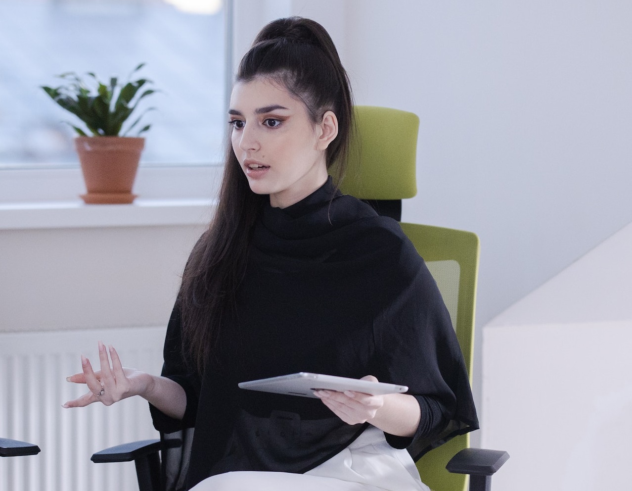 Young woman with long hair is explaining to other people in office meeting.