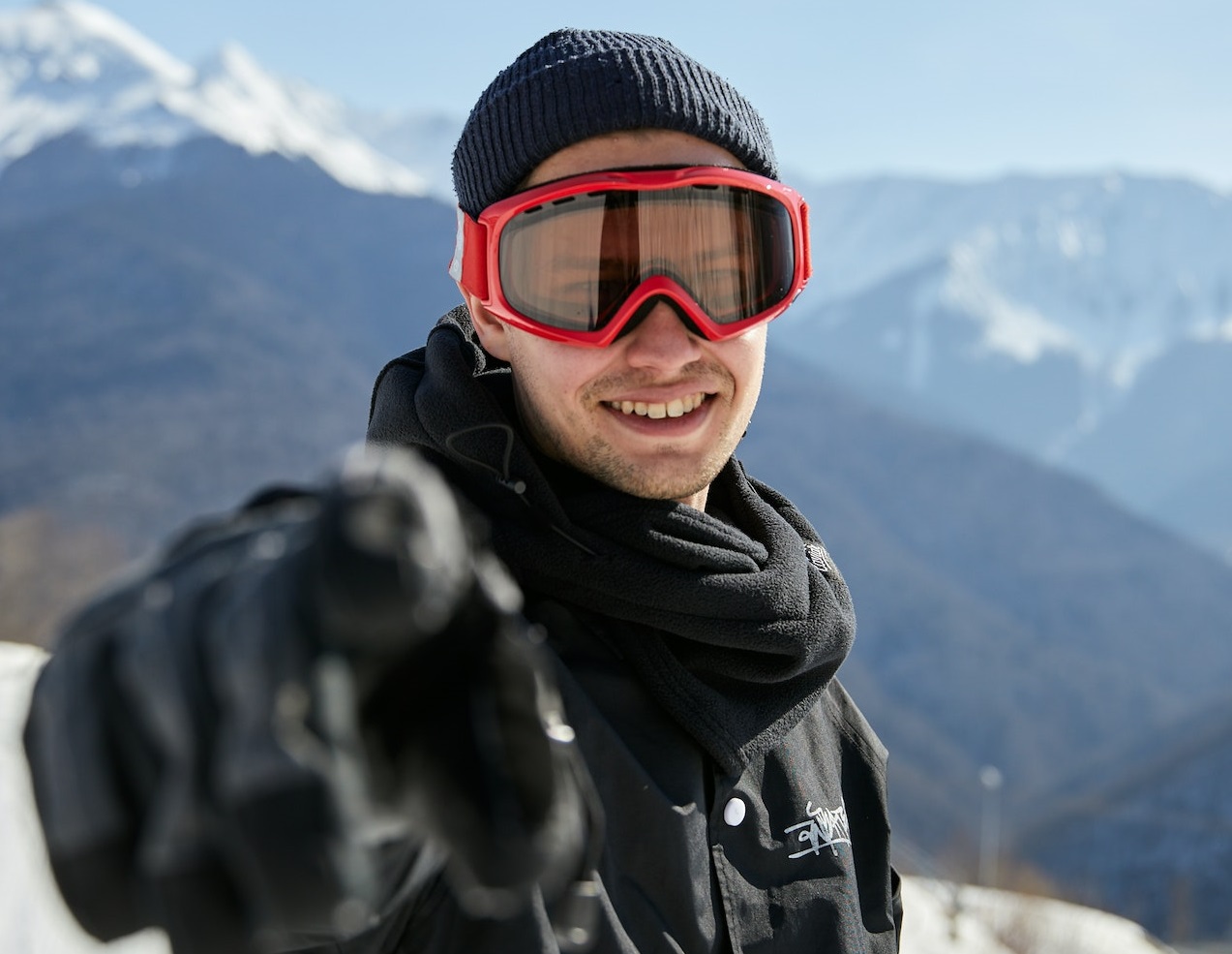 Young man is smiling and pointing to camera ,standing outside at snow.