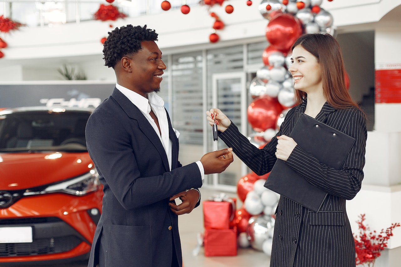 Young woman is giving a car key to a young man who is smiling.