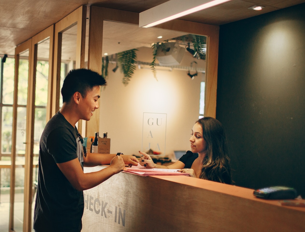 Man is standing in front of a front desk and talking with young woman with long hair.