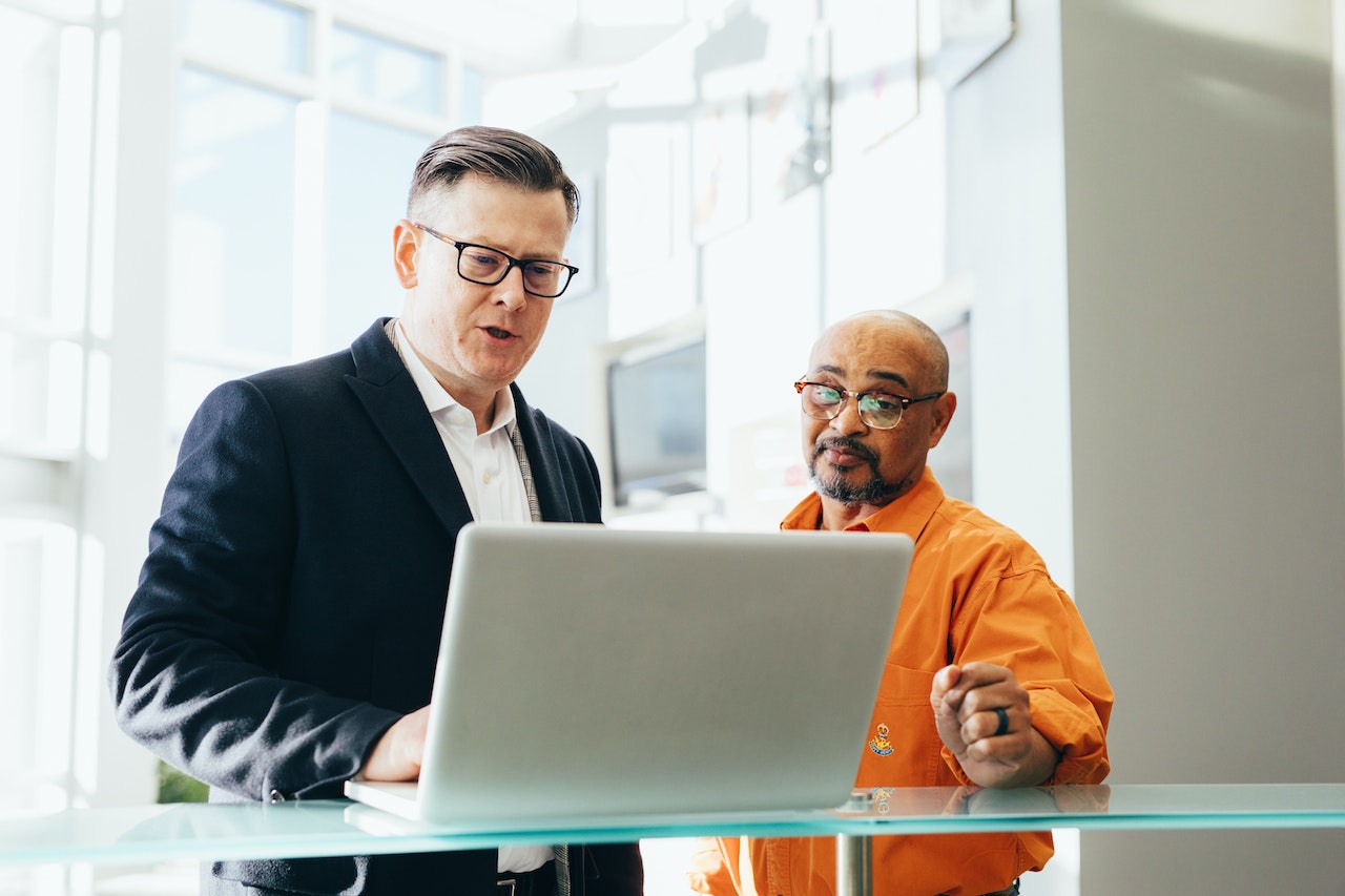 Business man is looking at lap top and talking with senior man standing next to him.