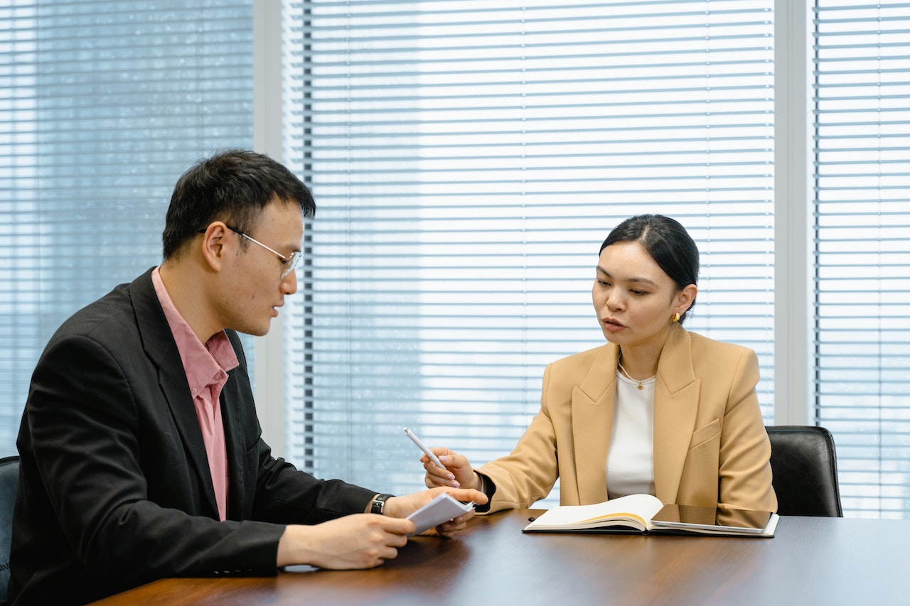 Woman is having a conversation wit man wearing black suit in office.