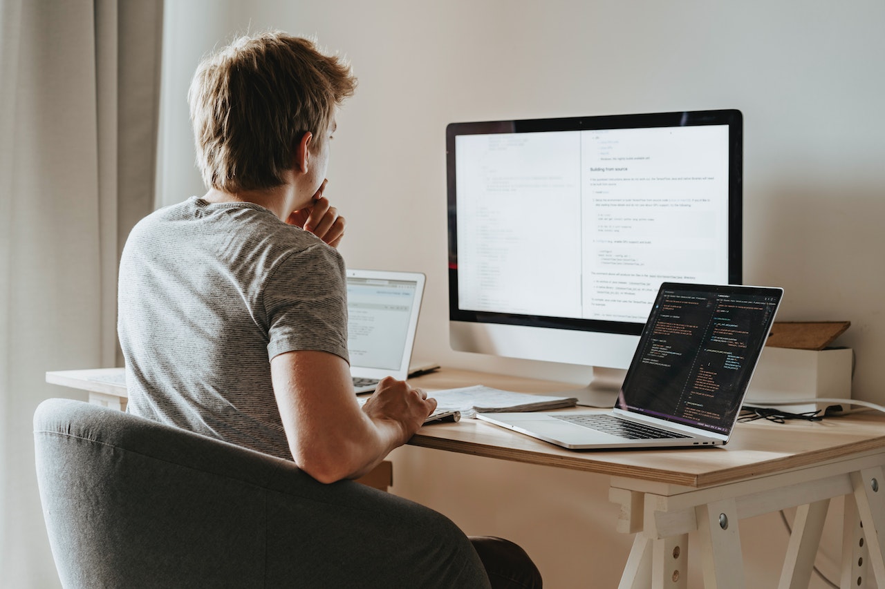 Young man is seating on desk and writing a code on PC.