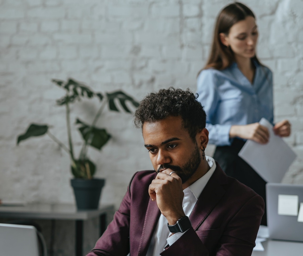 Man is seating and thinking on his desk with woman is standing behind him.