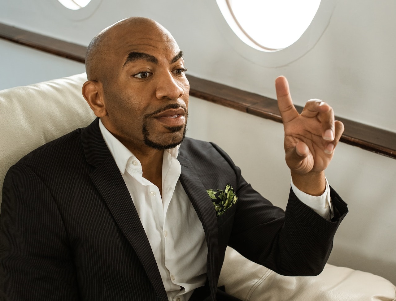 Young man is seating on private plane with hand up.