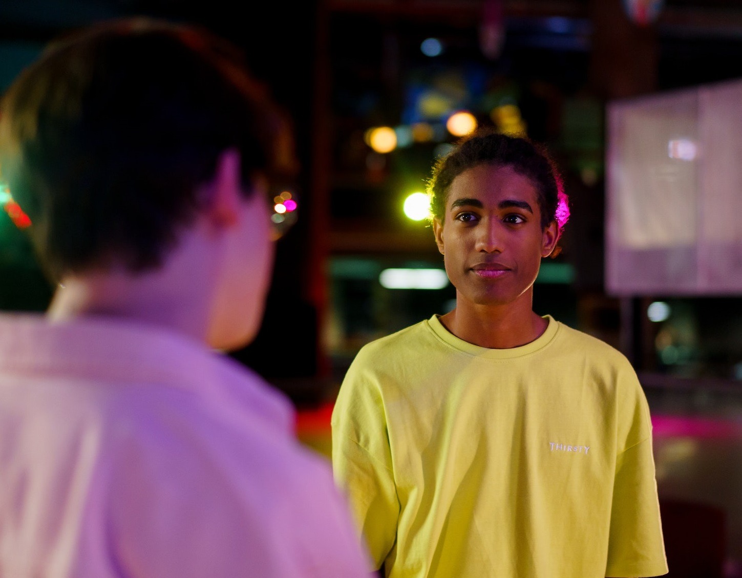 Young black man is looking at other male in dark room.