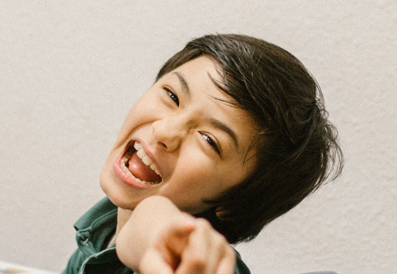 Kid is looking at camera, pointing with finger and laughing.