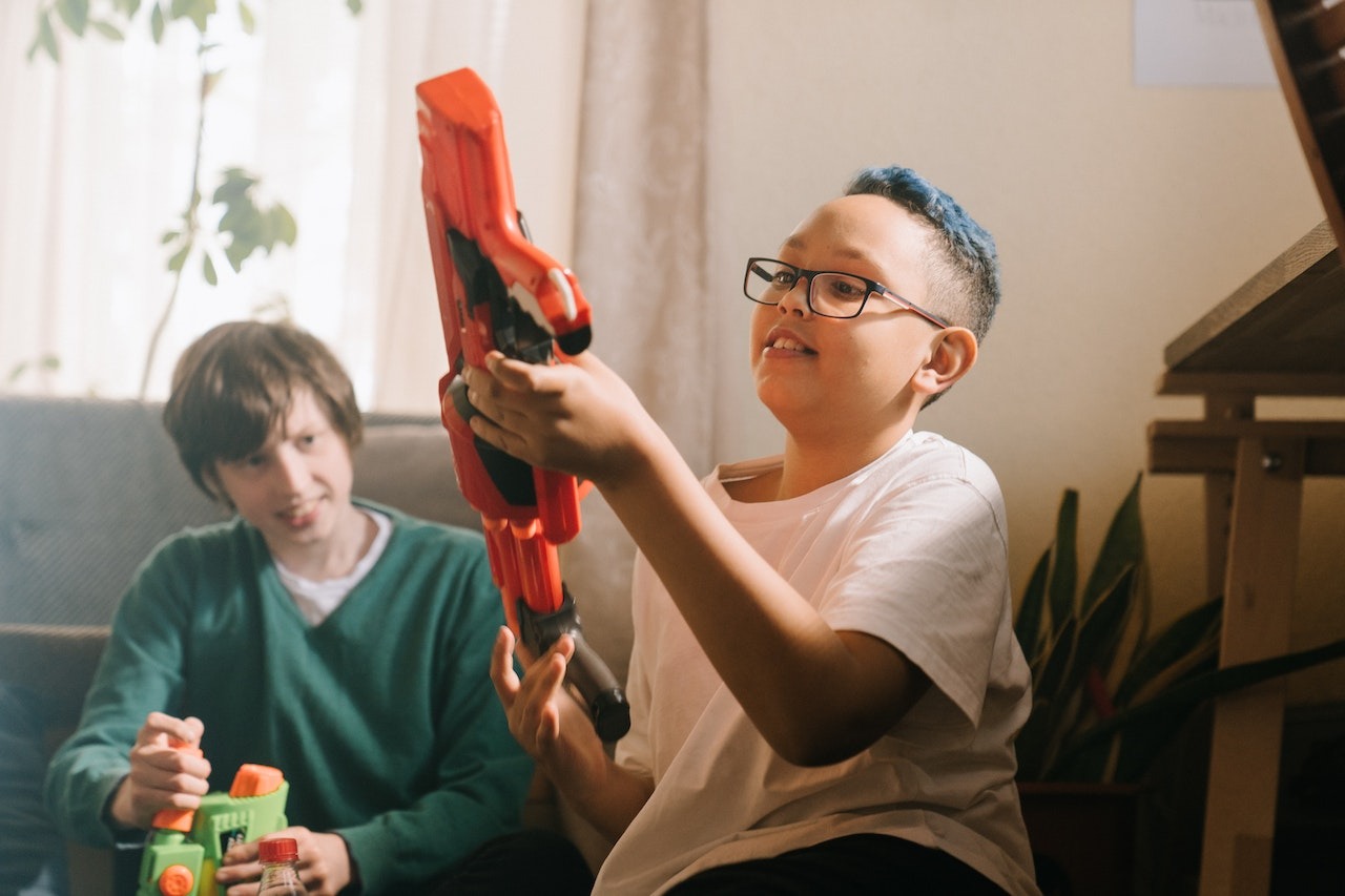 Young kids are seating in the room and playing with nerf gun.