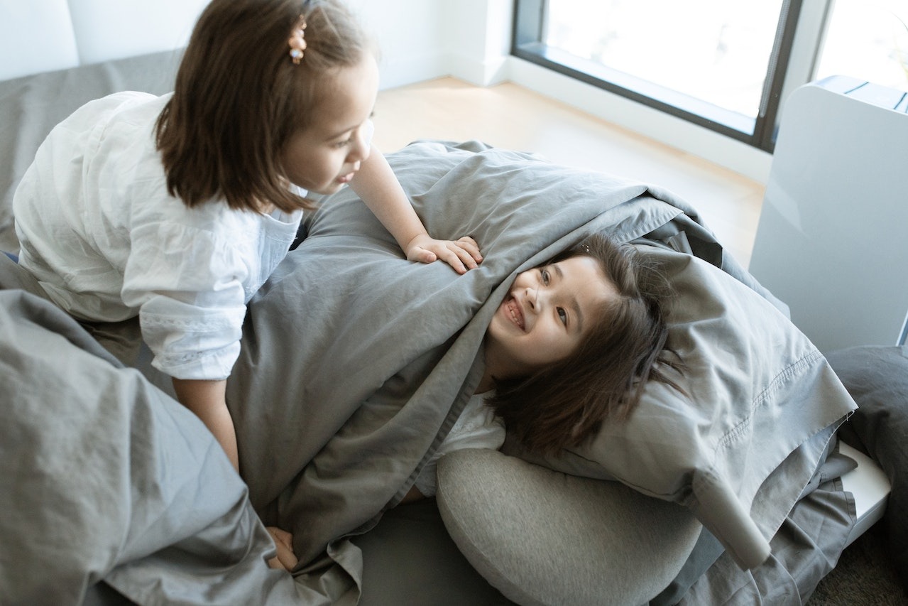 Two small girls are playing and laughing in the bed.