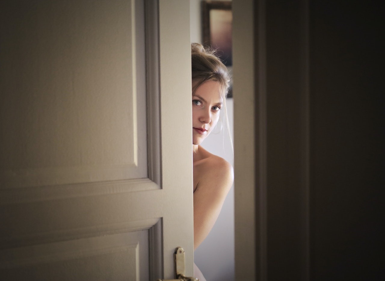 Young woman is looking at camera from behind white door.