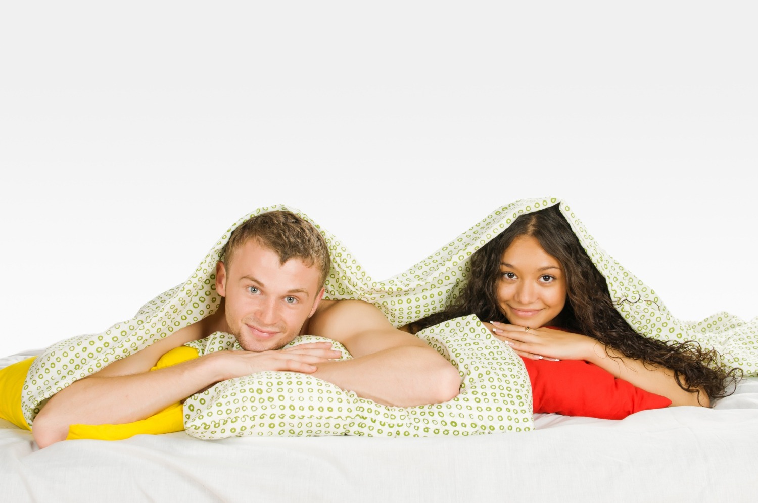 Young couple is hiding under the covers in bed.
