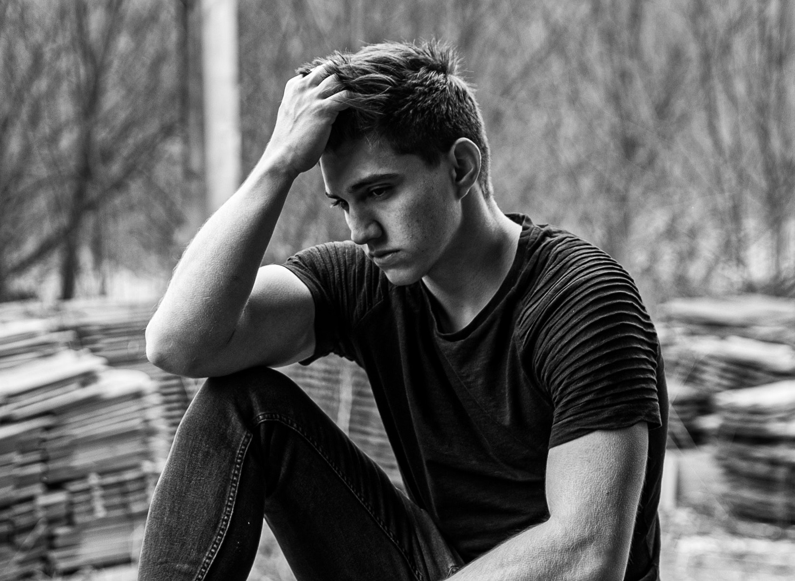 Young man is seating outside with sad face, looking down.