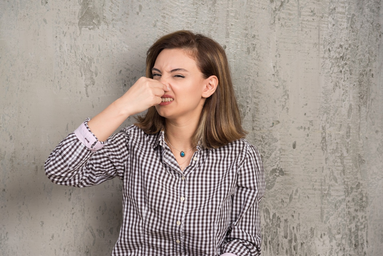 Young woman wearing B&W shirt is holding her nose and looking at side.