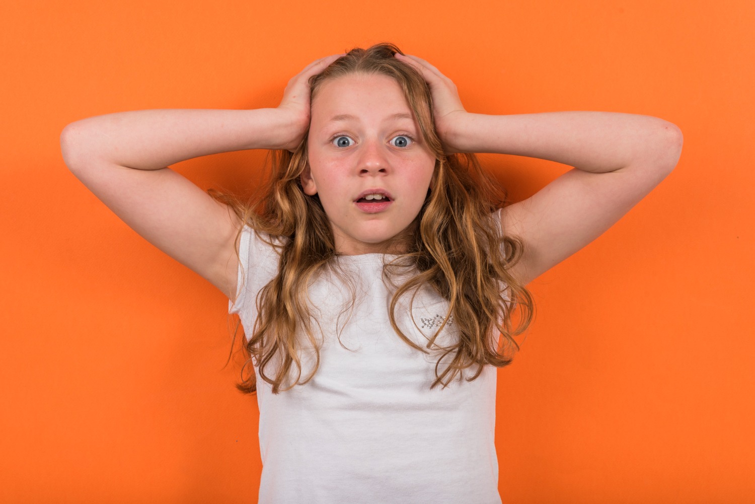 Small girl is looking shocked at camera on orange background.
