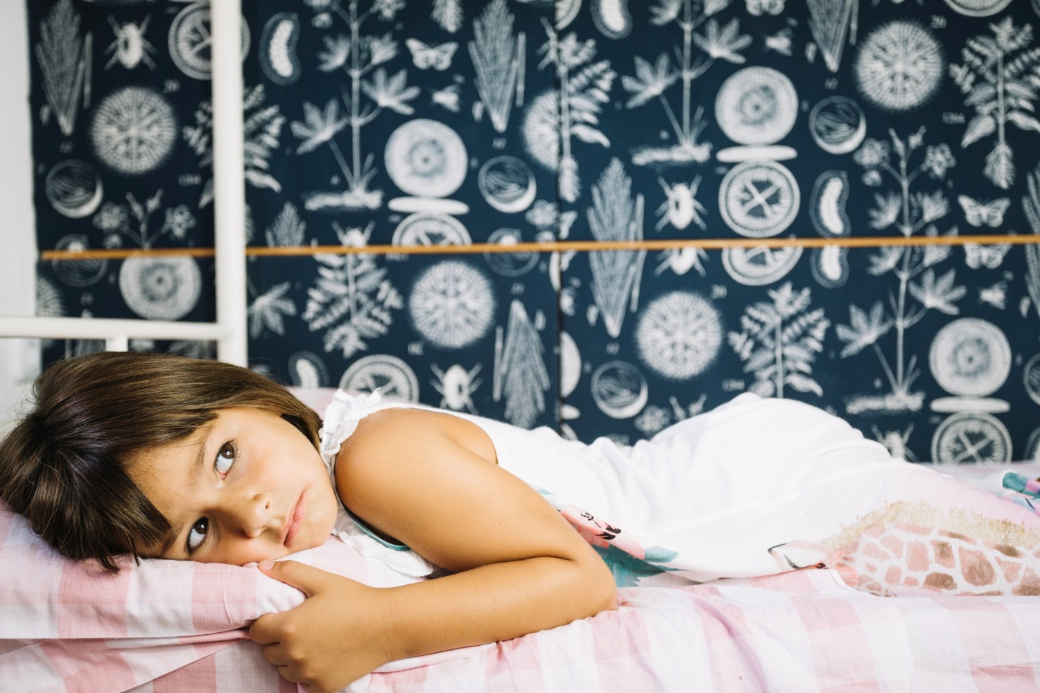 Small girl is laying on the bed, with upset face.