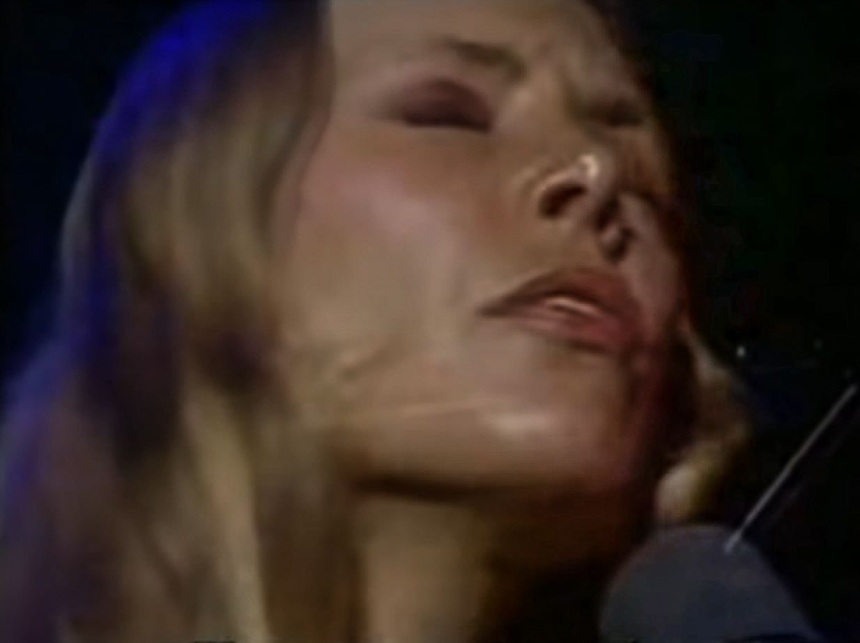 Screenshot: Joni Mitchell performing live in stage with closed eyes - from Joni Mitchell: A Woman of Heart and Mind (2003)
