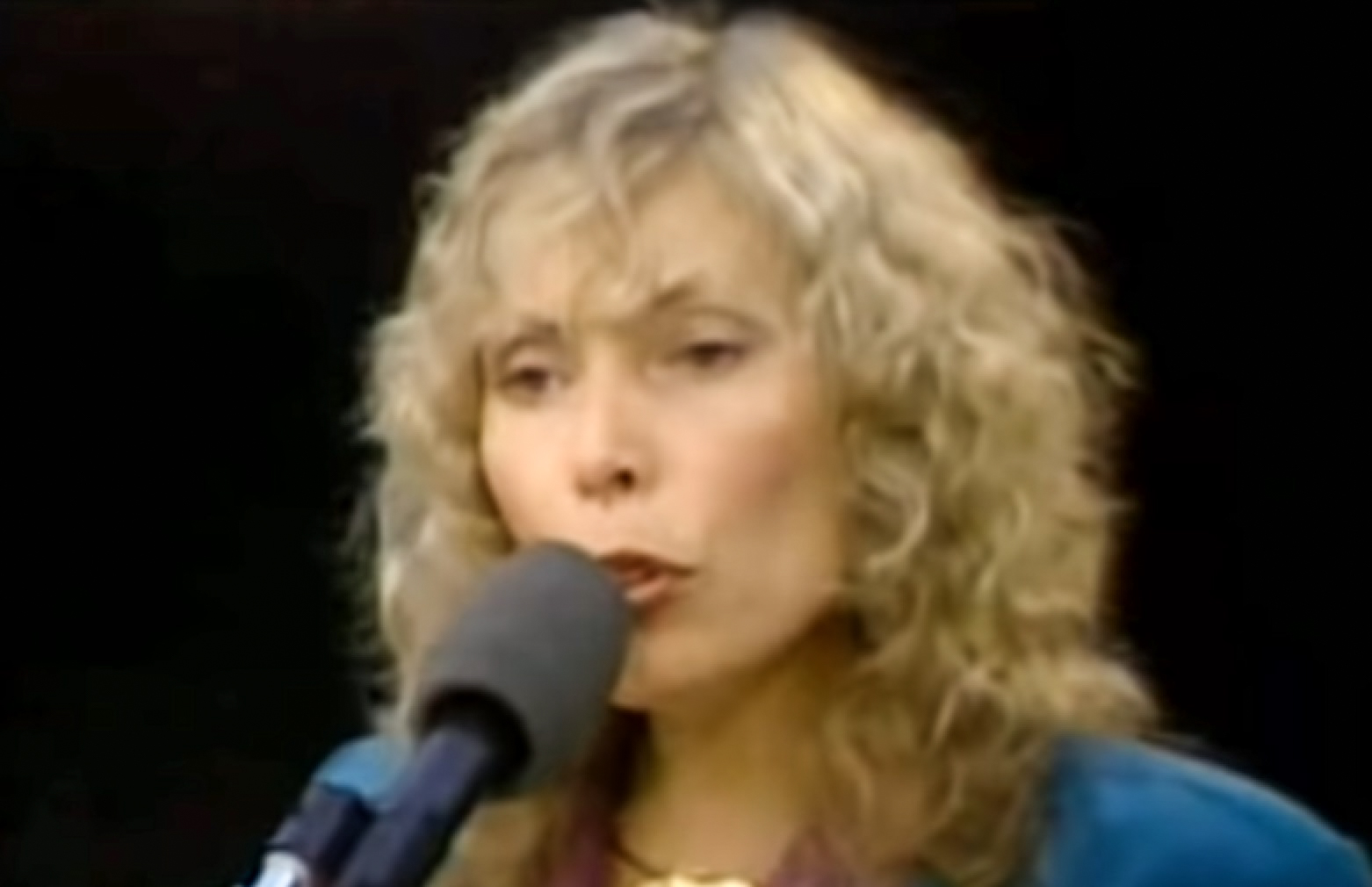 Screenshot: Joni Mitchell is looking at front and singing  - from Joni Mitchell: A Woman of Heart and Mind (2003)