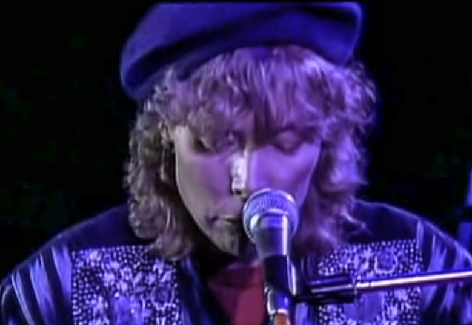 Screenshot: Joni Mitchell wearing black hat is looking at front and singing - from Joni Mitchell: A Woman of Heart and Mind (2003)