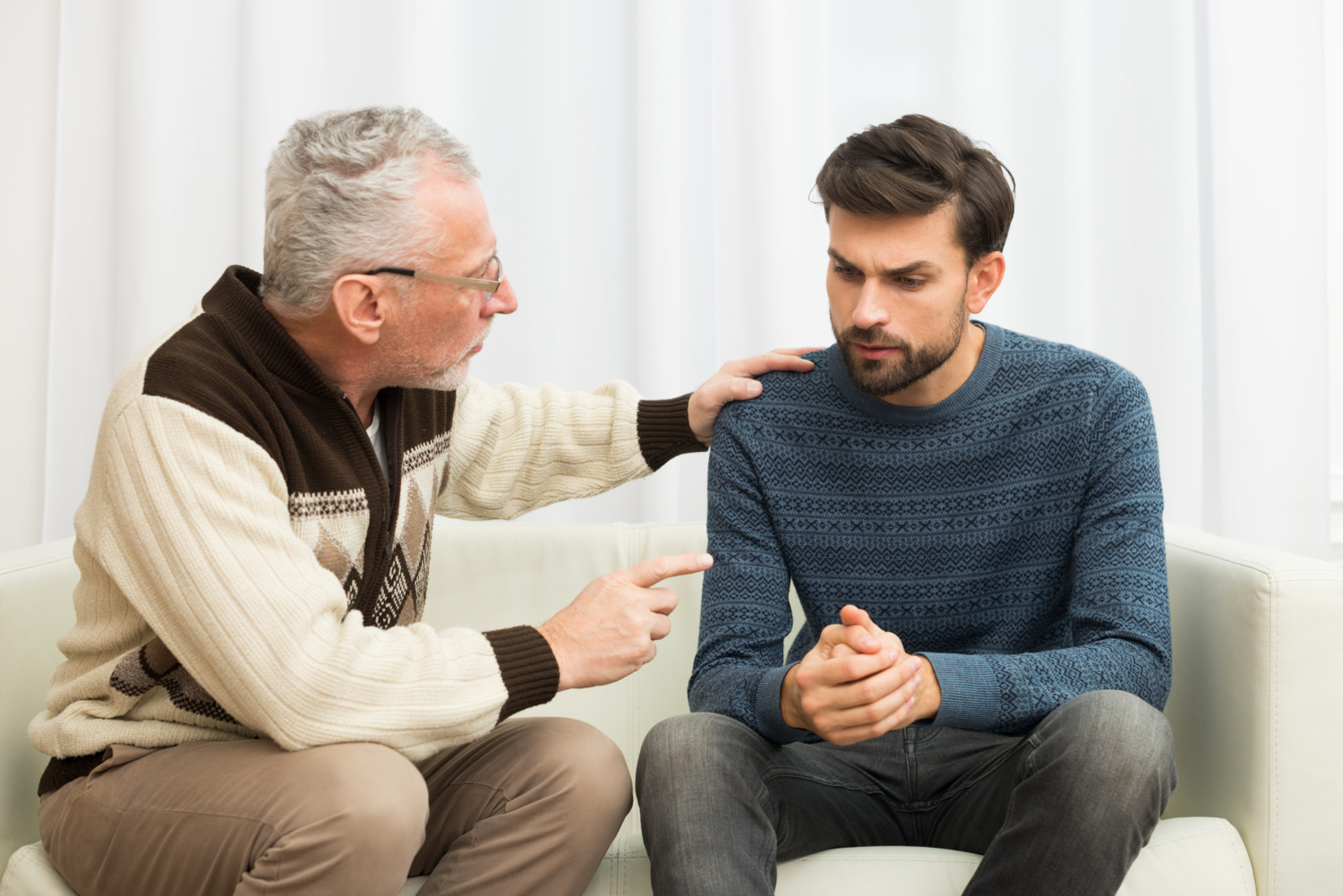 Father is talking with his son with sad face seating on the sofa.