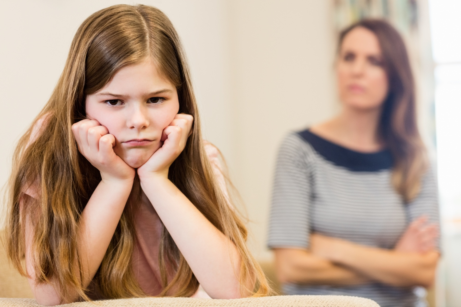 Young girl is seating upset with her mother standing behind her.