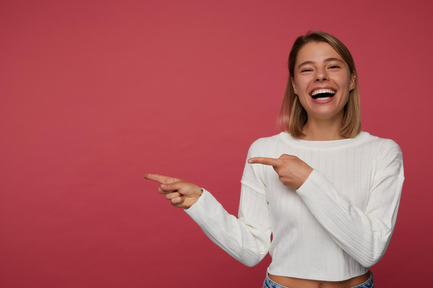 Woman wearing white sweater is laughing and pointing.