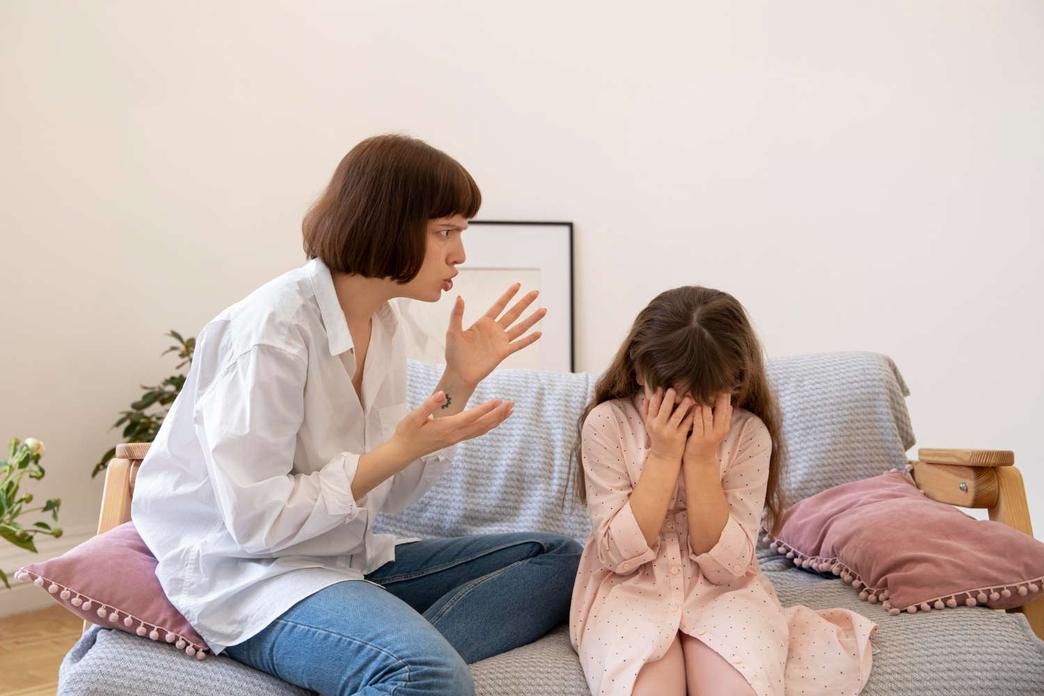 Young woman is yelling to a small girl in dress ,seating on the bed.