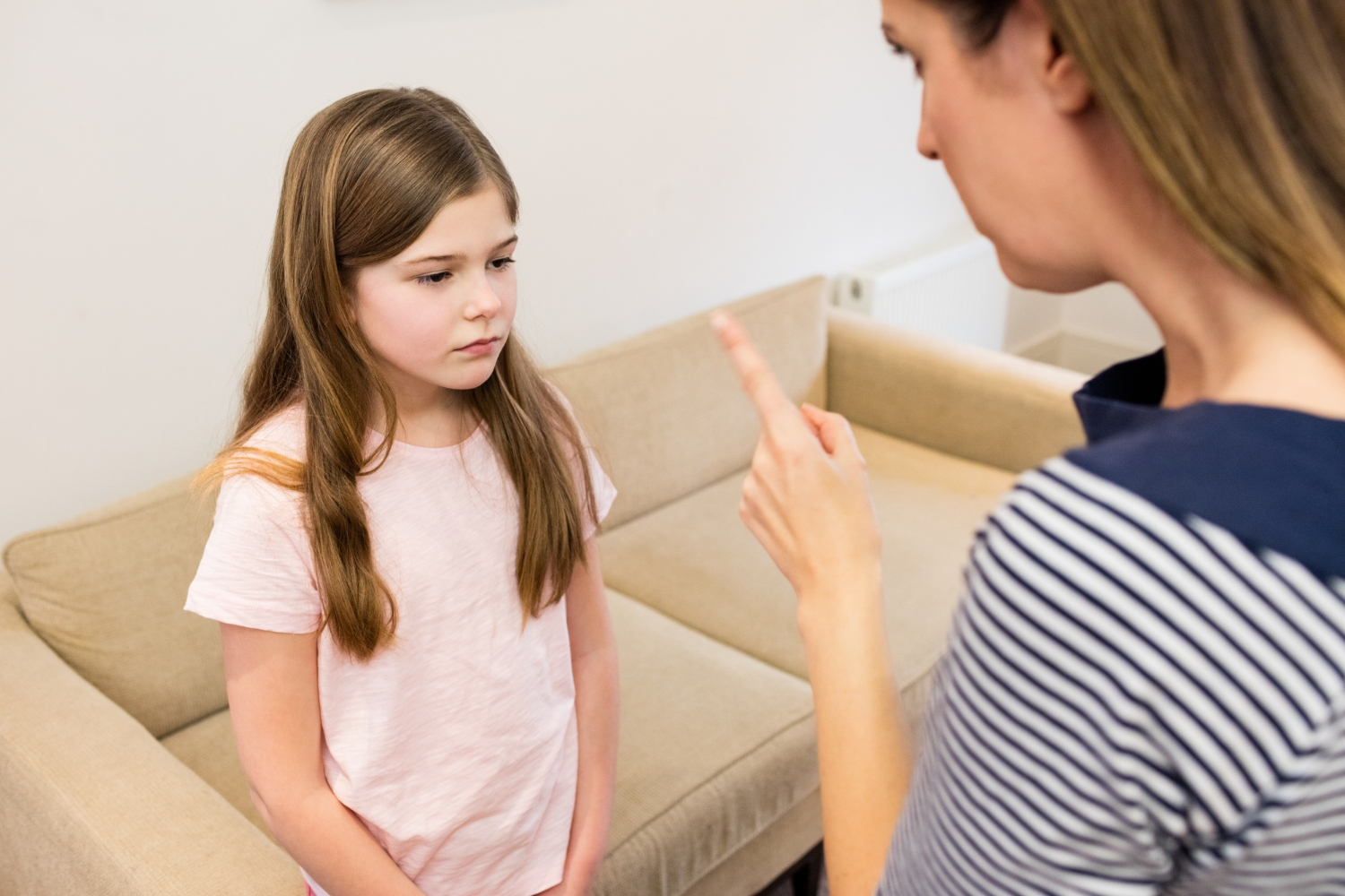 Mother wearing white and blue shirt is pointing to young daughter wearing pink shirt.