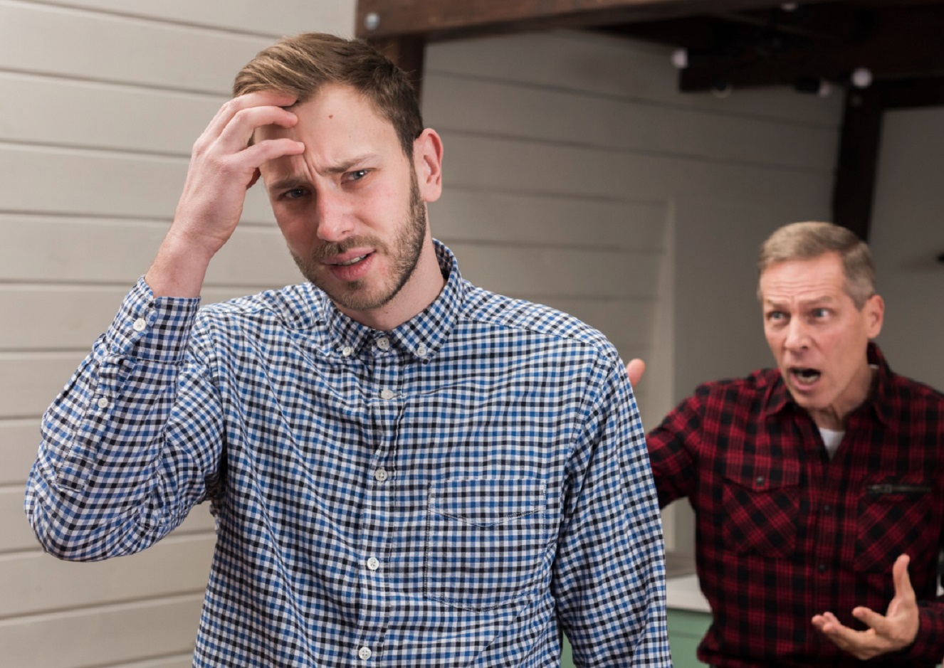 Angry old father screaming on son standing upset, holding his head.