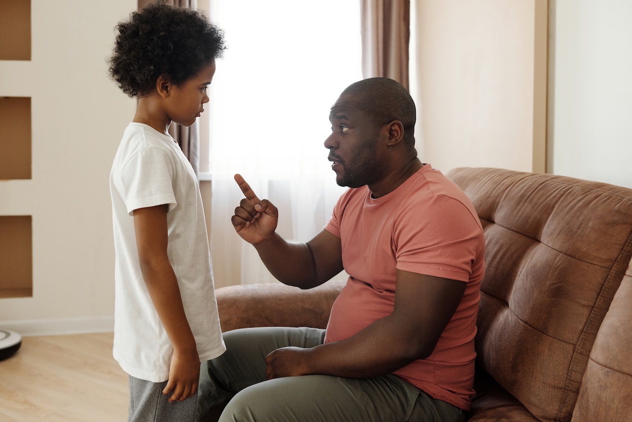Young kid is listening his father seating on the bed and talking.