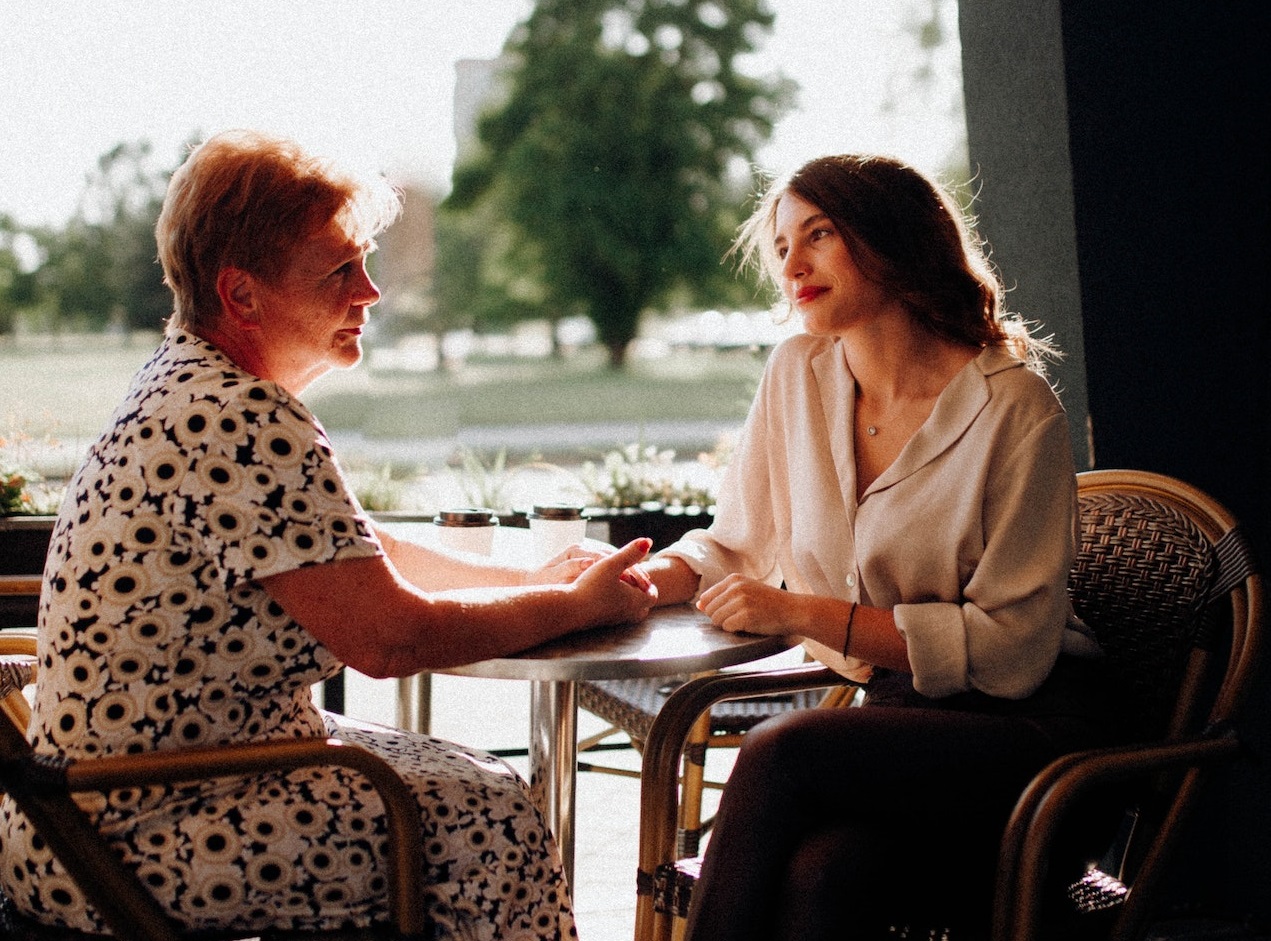 Senior woman is talking with young woman outside seating on the table.