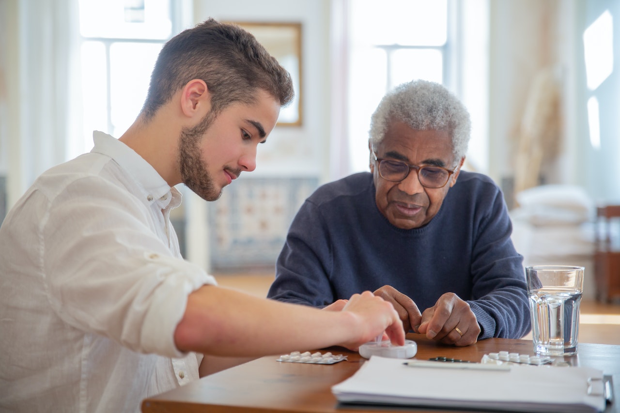 Young man is giving medications to an old man on the table.