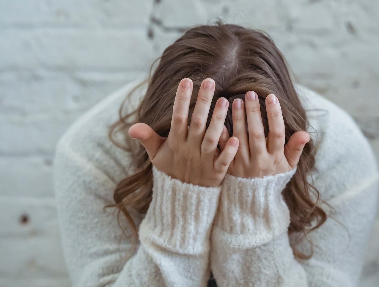 Woman is seating sad and holding her head with her arms.