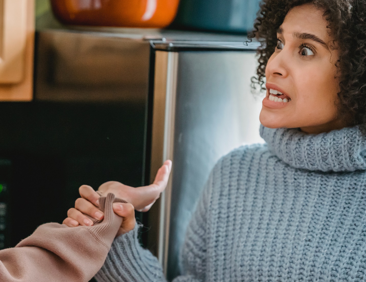Black woman wearing blue sweater is holding other person hand with angry face.